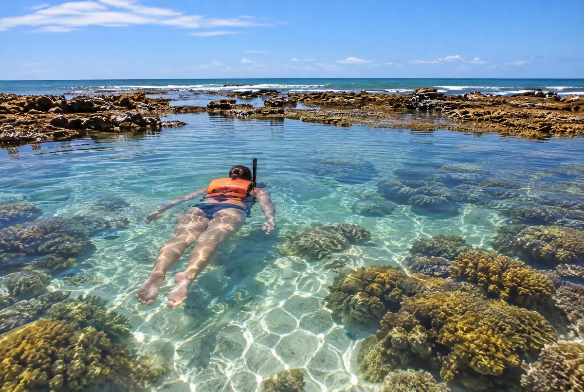 Pessoa de costas flutuando com máscara e colete laranja em piscina natural de água cristalina.